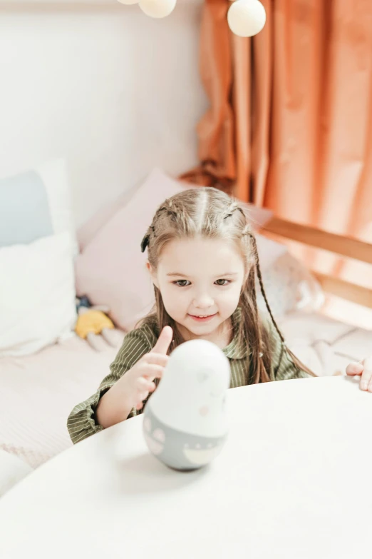 a little girl that is sitting at a table, holding up a night lamp, connectivity, an egg, with accurate features