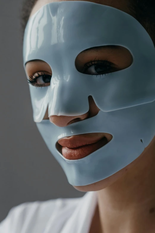 a woman with a blue mask on her face, glowing porcelain skin, on a gray background, clear [bronze] face, pokimane