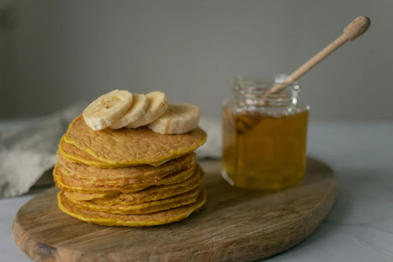 a stack of pancakes sitting on top of a wooden cutting board, by Alice Mason, pexels, jar of honey, banana, ochre, brilliantly coloured