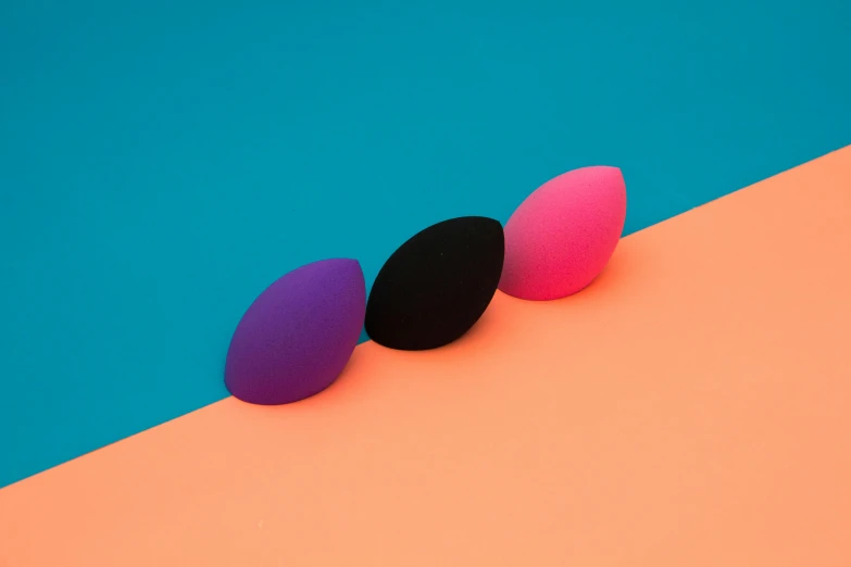 three makeup sponges on an orange and blue background, by Paul Bird, magenta colours, lenses, 84mm), various posed