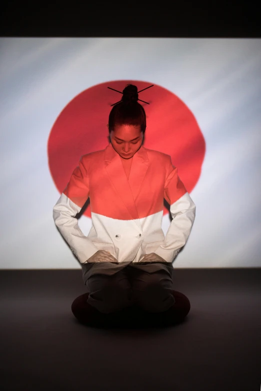 a woman sitting on the ground in front of a large screen, inspired by Koson Ohara, unsplash, patriotism, performance art, karate, official photo