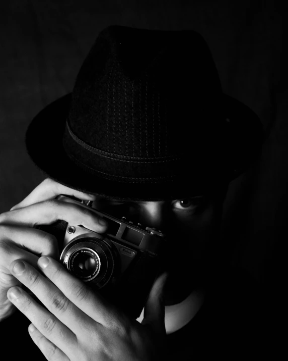 a man holding a camera up to his face, a black and white photo, by Adam Marczyński, noir detective and a fedora, looking at you, art : : professional photograph, medium format