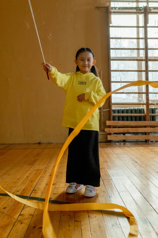 a little girl standing on top of a hard wood floor, inspired by Wang Zhongyu, gutai group, wearing a yellow hoodie, floggers, promo image, ( ( theatrical ) )