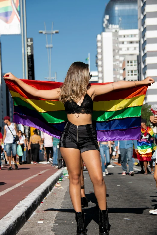 a woman walking down a street holding a rainbow flag, trending on unsplash, sao paulo, wearing a crop top, crowds, brown