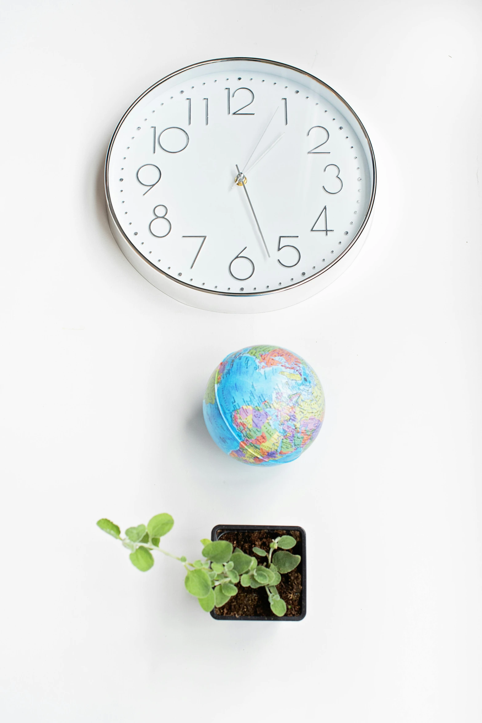 a clock sitting on top of a white wall next to a plant, earth globe on top, floating objects, high angle, product shot