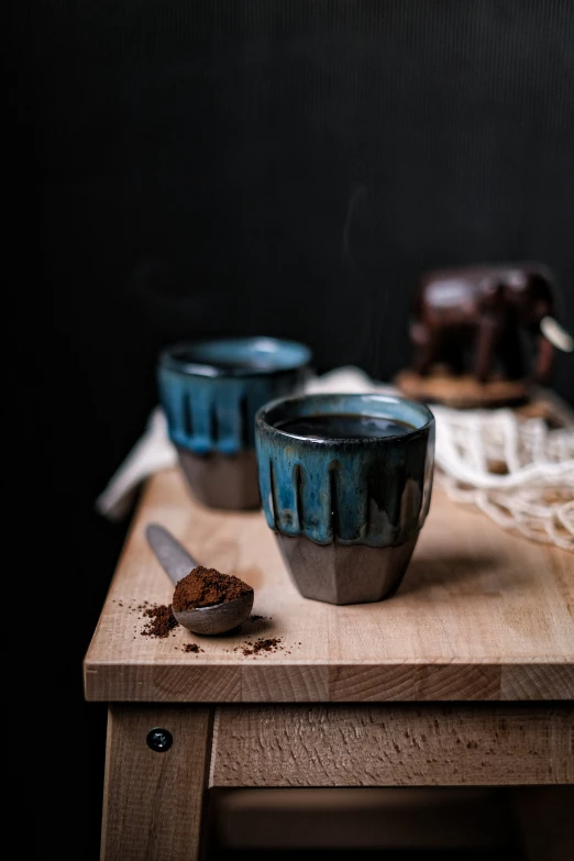 a couple of cups sitting on top of a wooden table, a still life, inspired by Muggur, unsplash, hurufiyya, chocolate. rugged, dark teal, square, made of glazed