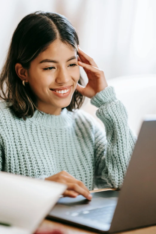 a woman sitting at a table using a laptop computer, trending on pexels, renaissance, south east asian with round face, smiling young woman, wearing a green sweater, avatar image