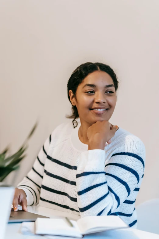 a woman sitting at a table with a laptop, a character portrait, by Lily Delissa Joseph, pexels contest winner, wearing stripe shirt, in white turtleneck shirt, smiling kindly, jayison devadas