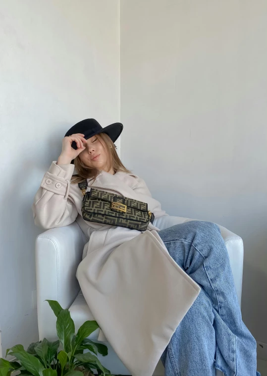 a woman sitting on a couch next to a potted plant, by Nina Hamnett, trending on instagram, happening, beige fedora, trending on r/streetwear, fluid bag, thumbnail