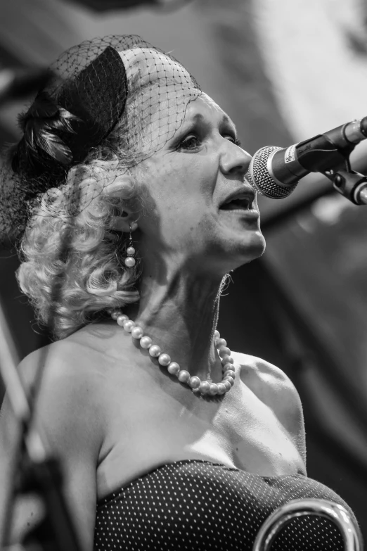 a woman in a dress singing into a microphone, a black and white photo, by Dave Melvin, strings of pearls, square, high quality image, colours