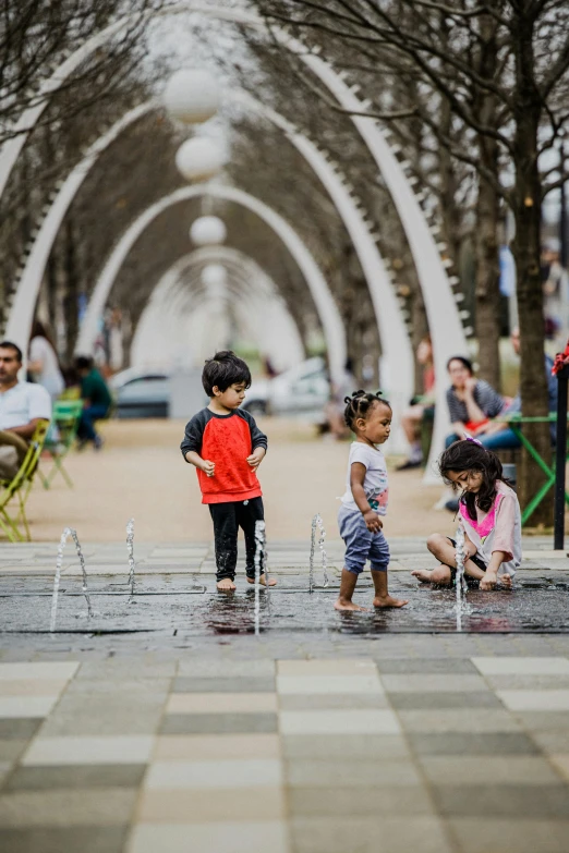 a group of children playing in a fountain, inspired by Myles Birket Foster, pexels contest winner, interactive art, steel archways, white sweeping arches, people walking around, square