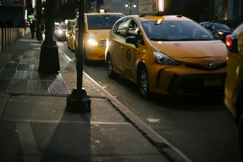 a city street filled with lots of traffic next to tall buildings, by Carey Morris, pexels contest winner, taxi, lamps on ground, yellow and black, square