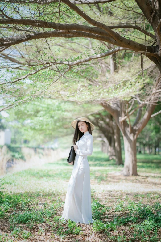 a woman in a white dress standing under a tree, by Tan Ting-pho, unsplash, straw hat and overcoat, square, ao dai, lawn