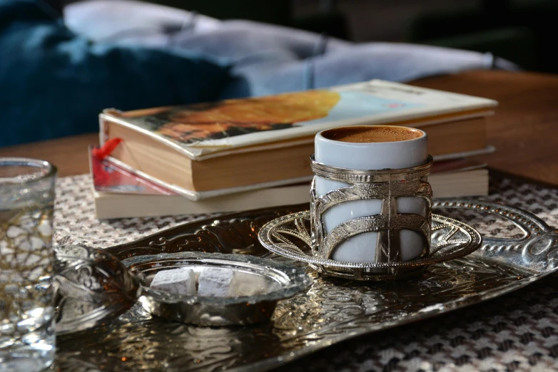 a silver tray sitting on top of a wooden table, by Riad Beyrouti, pexels contest winner, arabesque, coffee cups, silver，ivory, with one vintage book on a table, melting