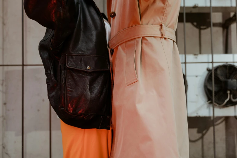 a couple of women standing next to each other, trending on pexels, visual art, leather trench coat, pink and orange, half male and half female, extra close-up