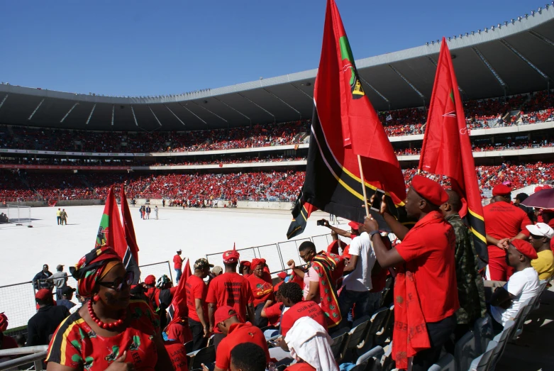 a group of people holding flags in a stadium, by Hubert van Ravesteyn, pexels contest winner, hurufiyya, it has a red and black paint, zulu, 2 5 6 x 2 5 6 pixels, sitting down