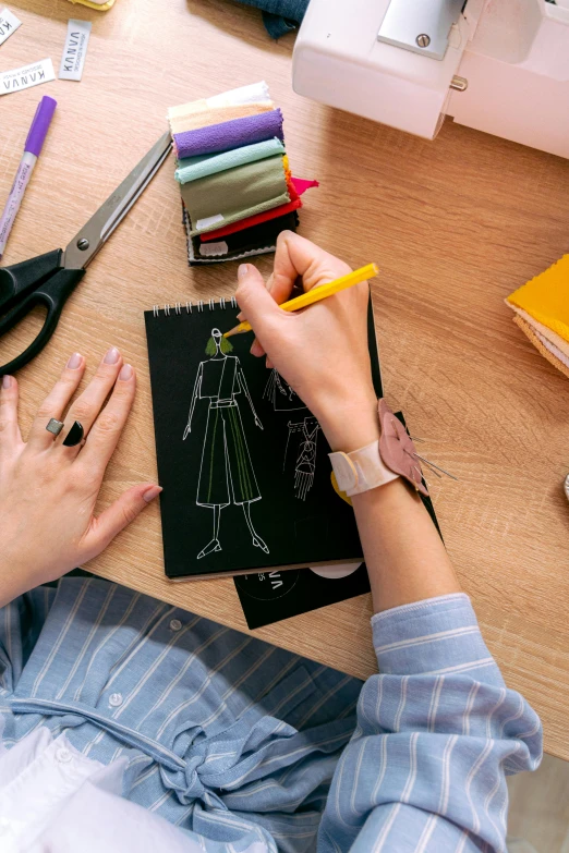 a woman sitting at a table working on a piece of paper, a drawing, trending on pexels, clothing design, 9 9 designs, on dark paper, teacher