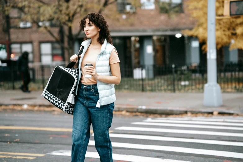 a woman standing in the middle of a cross walk, by Nina Hamnett, trending on pexels, holding a boba milky oolong tea, outfit : jeans and white vest, curly haired, holding mesh bag with bagels