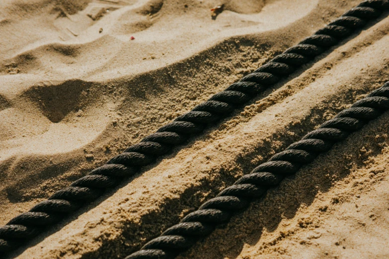 a black rope laying on top of a sandy beach, heavy lines, thumbnail, units, brown