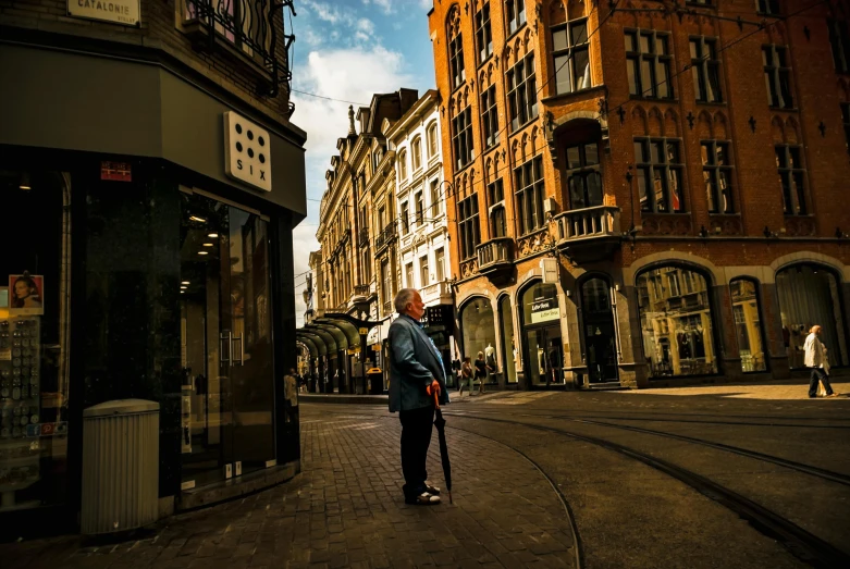 a man walking down a street next to tall buildings, a photo, by Jan Tengnagel, pexels contest winner, happening, old shops, holding a cane, helmond, thumbnail