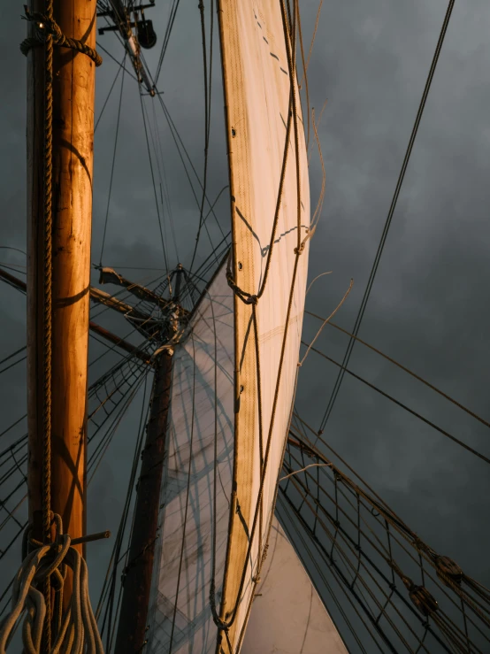 a close up of a sail on a body of water, by Jan Tengnagel, unsplash contest winner, romanticism, against a stormy sky, looking up, a wooden, overcast gray skies