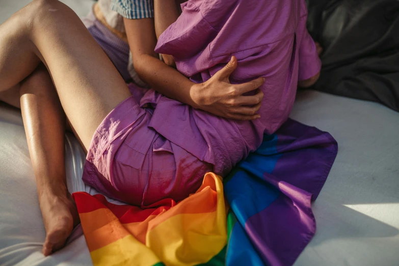 a woman sitting on top of a bed covered in a blanket, trending on pexels, happening, pride parade, holding each other, straya, physical : tinyest midriff ever
