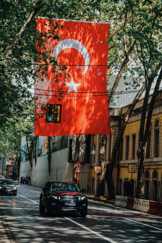 a group of cars driving down a street next to tall buildings, an album cover, inspired by Niyazi Selimoglu, pexels contest winner, hurufiyya, flag, turkey, square, color image