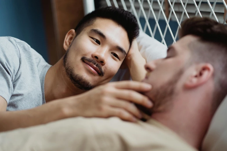 a man laying in bed next to another man, trending on pexels, square masculine jaw, asian female, multicoloured, supportive