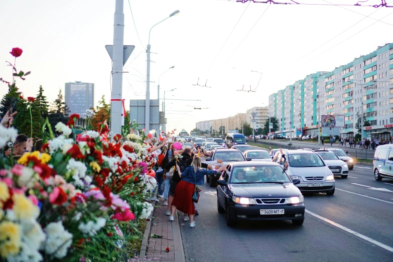 a group of people walking down a street next to a bunch of flowers, lada, multiple stories, cars and people, profile image