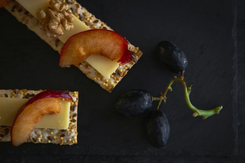 a black plate topped with crackers covered in cheese and fruit, inspired by Pieter Claesz, pexels, rectangle, food advertisement, 120mm, thumbnail