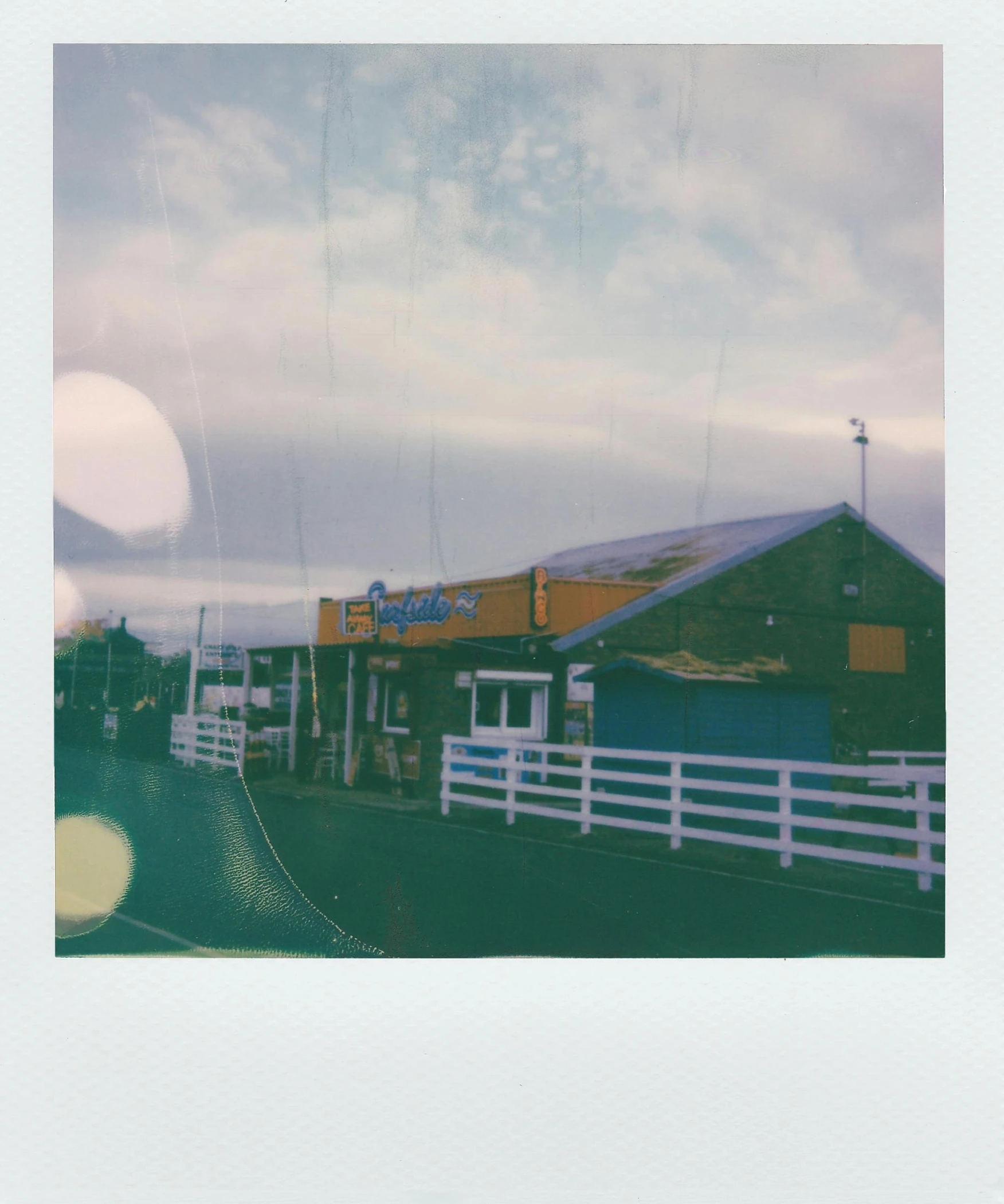 a picture of a building with a fence in front of it, a polaroid photo, unsplash, seaside, walton's five and dime, dreamworld, slightly pixelated