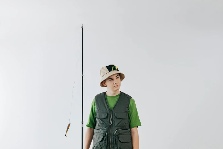 a boy in a hat is holding a fishing rod, an album cover, unsplash, realism, model is wearing techtical vest, ignant, some green, studio