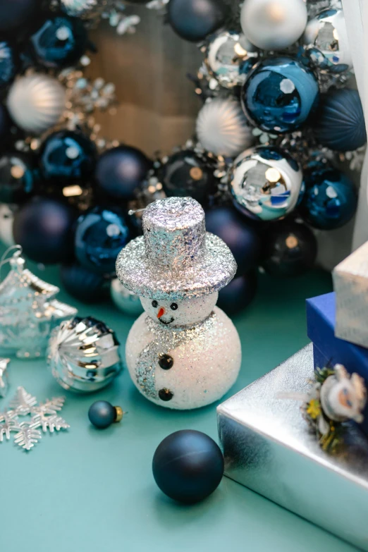 a snowman sitting on top of a table next to a pile of presents, silver and blue color schemes, zoomed in, thumbnail, ornaments