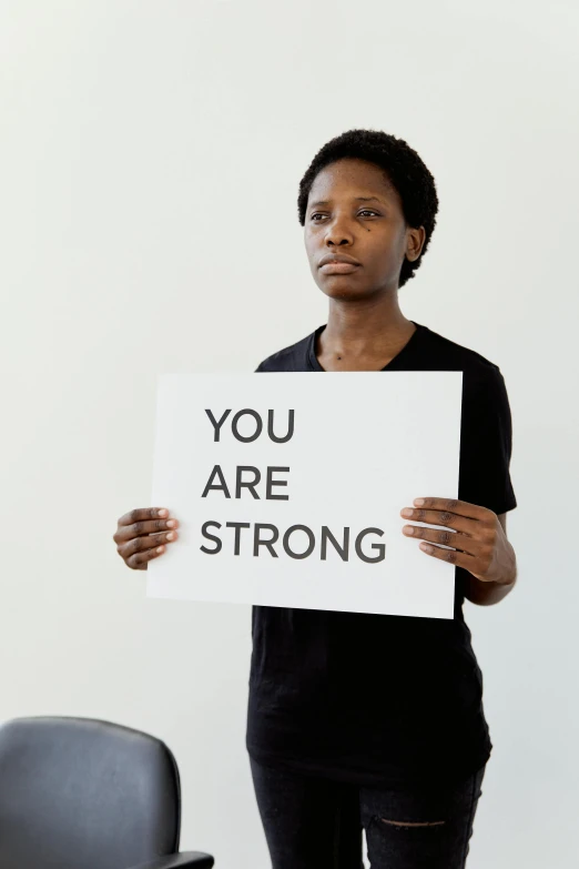 a woman holding a sign that says you are strong, a black and white photo, dark-skinned, lgbt, recovering from pain, standing together