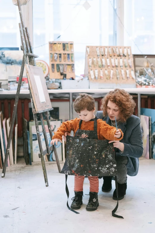 a woman kneeling next to a child in an art studio, by Quirijn van Brekelenkam, pexels contest winner, arbeitsrat für kunst, rectangle, artist wearing overalls, material art, graphic print