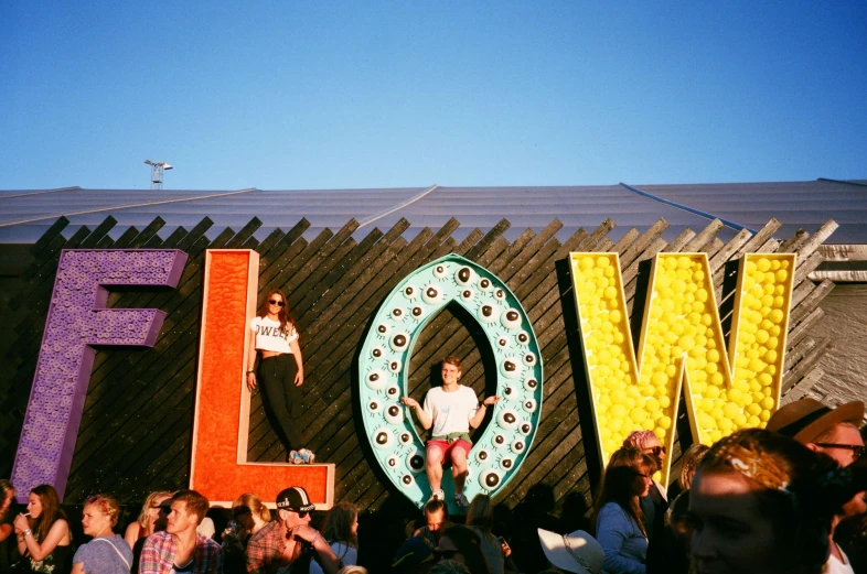 a group of people standing in front of a large love sign, by Rachel Reckitt, trending on unsplash, festivals, giant flowers, sitting down, looking from slightly below