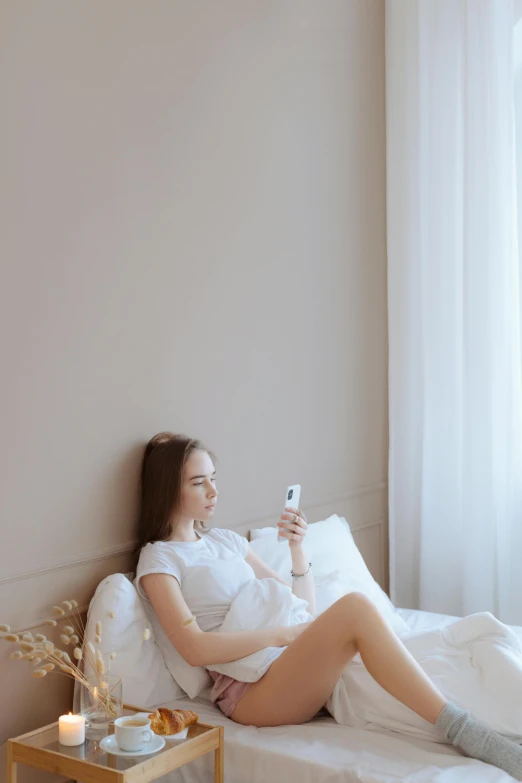a woman sitting on top of a bed next to a window, trending on pexels, cell phone, in white clothes, russian girlfriend, on a couch