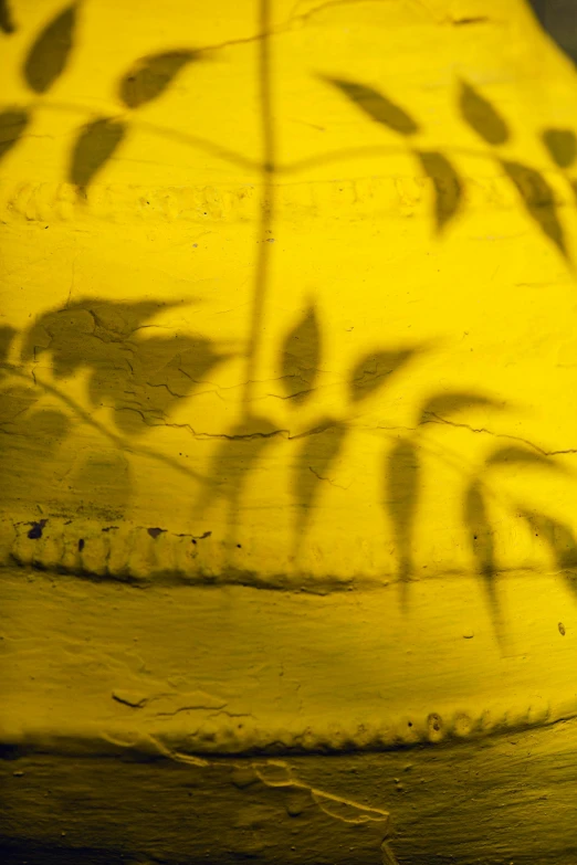 a yellow vase sitting on top of a wooden table, a picture, inspired by Andy Goldsworthy, lyrical abstraction, trees cast shadows on the wall, detail shot, stencil, glowing leaves