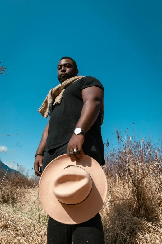 a man standing in a field with a hat, an album cover, pexels contest winner, alluring plus sized model, ( ( dark skin ) ), sunny day time, teddy fresh