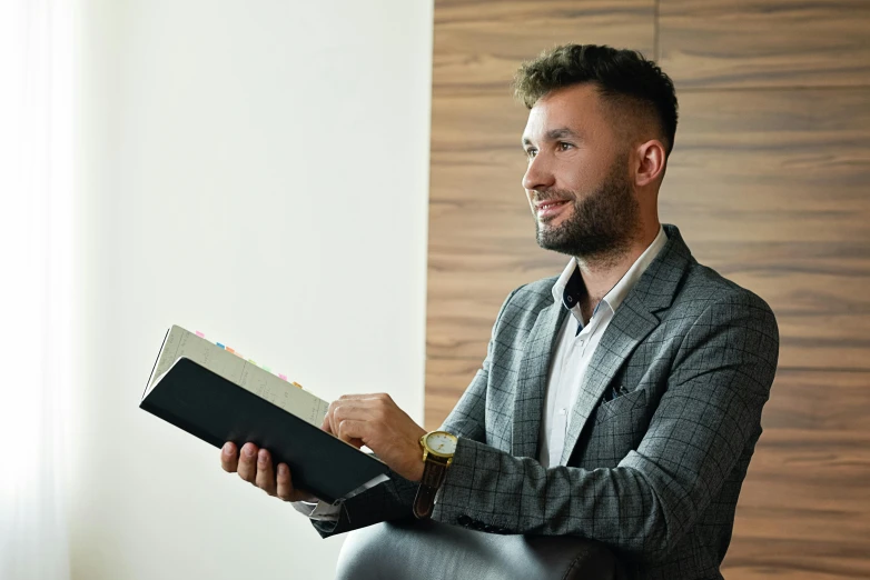 a man sitting in a chair reading a book, wearing business casual dress, hasbulla magomedov, ready for a meeting, smiling man