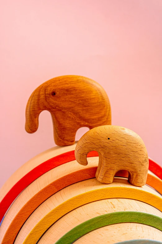 a wooden elephant standing on top of a rainbow, by Sam Havadtoy, light red and orange mood, 2 animals, medium close up, wheels