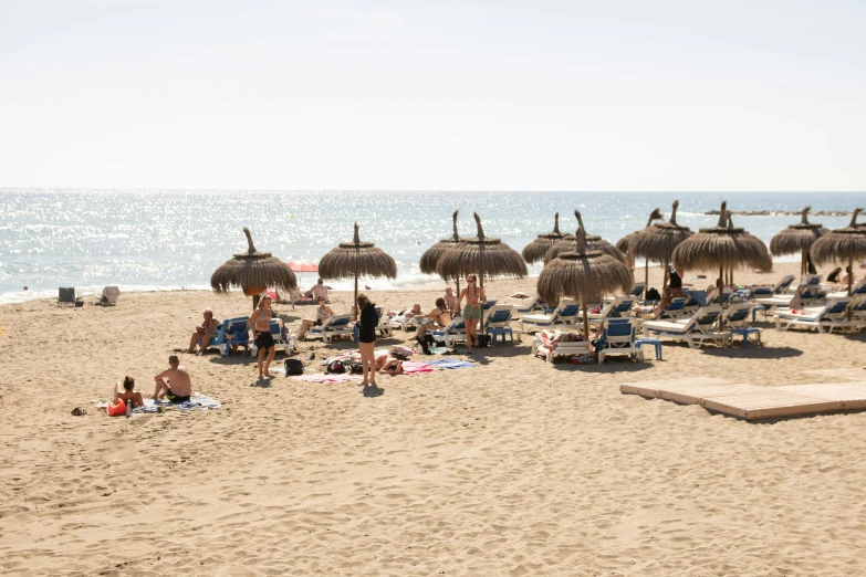 a group of people sitting on top of a sandy beach, marbella, thatched roofs, white beaches, heat shimmering