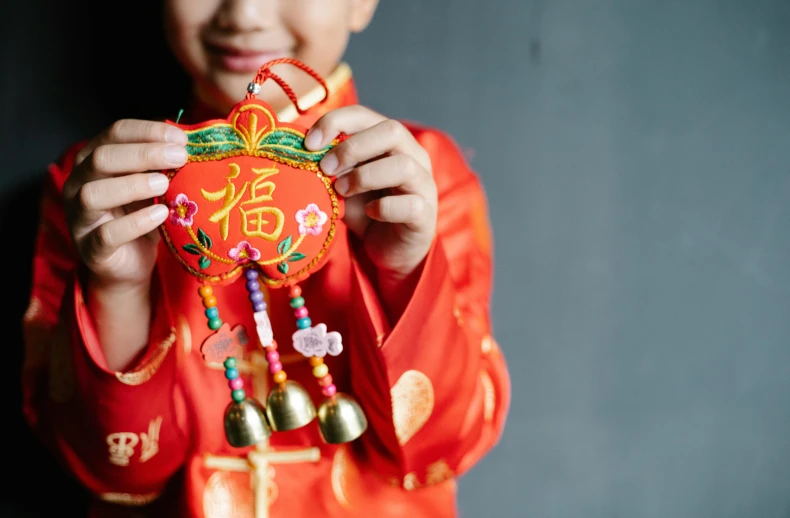 a close up of a person holding a small object, inspired by Ni Duan, trending on unsplash, celebration costume, hanging, little boy, very ornamented