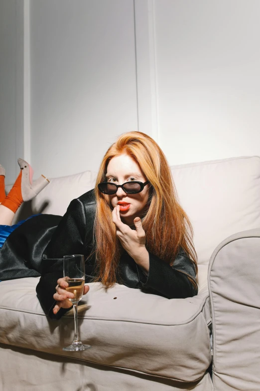 a woman laying on a couch with a glass of wine, inspired by Nan Goldin, trending on reddit, pop art, very long orange hair, giving the middle finger, ellie bamber, terry richardson
