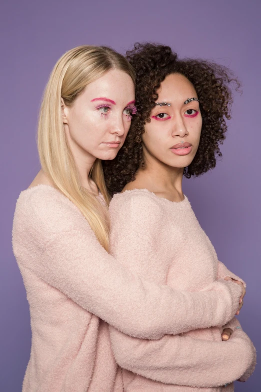 two women standing next to each other in front of a purple background, inspired by Vanessa Beecroft, trending on pexels, lavender and pink eyes, promotional image, mixed race, a blond