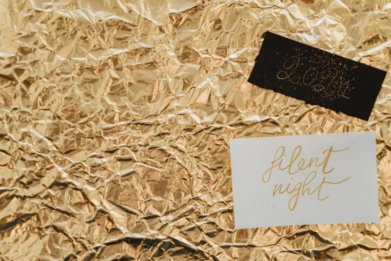 a piece of foil sitting on top of a table, by Julia Pishtar, pexels contest winner, mail art, night!, gold linens, lettering, cardstock