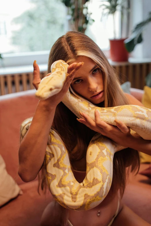 a woman holding a snake over her head, trending on pexels, with long blond hair, sitting on a couch, 2 animals, 1 8 yo