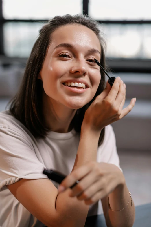 a woman sitting on the floor talking on a cell phone, trending on pexels, photorealism, round chin black eyeliner, putting makeup on, happily smiling at the camera, heavy mascara