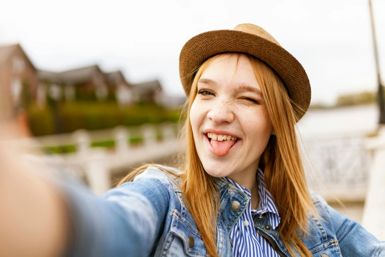 a woman taking a selfie with her cell phone, trending on pexels, tongue out, a redheaded young woman, caracter with brown hat, rated t for teen