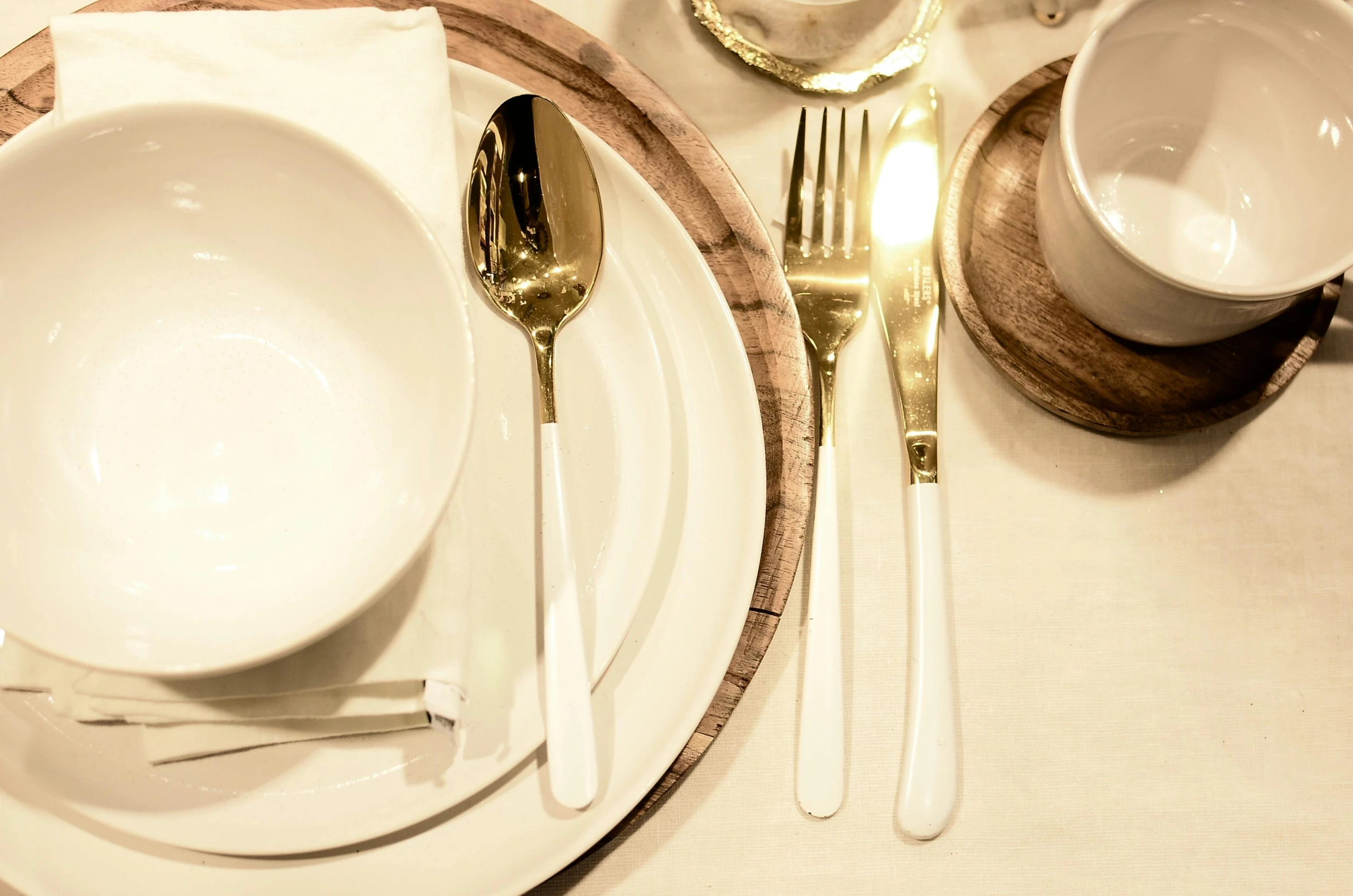 a white plate topped with a bowl and silverware, on a table, golden eal, bespoke, medium close up